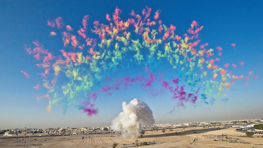 A rainbow made of colourful puffs of smoke in the blue sky over a dry landscape.