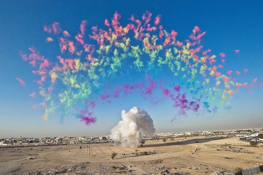 A rainbow made of colourful puffs of smoke in the blue sky over a dry landscape.