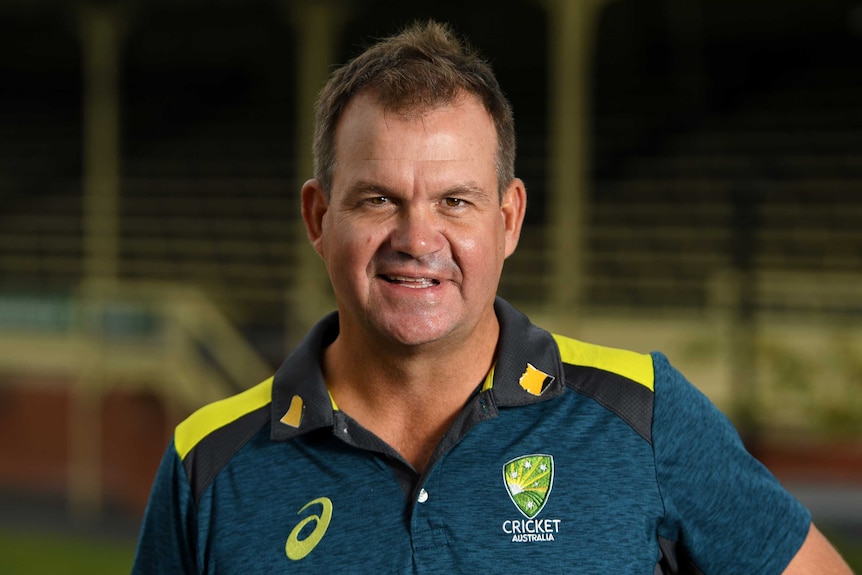 The coach of Australia's women's cricket team stands smiling in front of a grandstand.