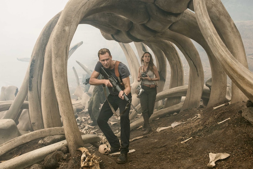 Tom Hiddleston and Brie Larson walk through a giant monster skeleton in Kong: Skull Island.
