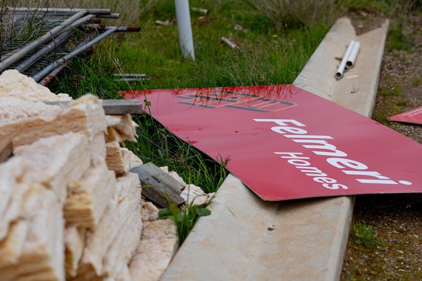A red sign reading Felmeri Homes on grass next to construction materials