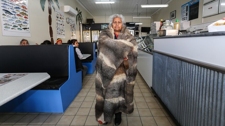 A defiant Esther Kirby stands in the middle of a fish and chip shop wrapped in her possum skin cloak.