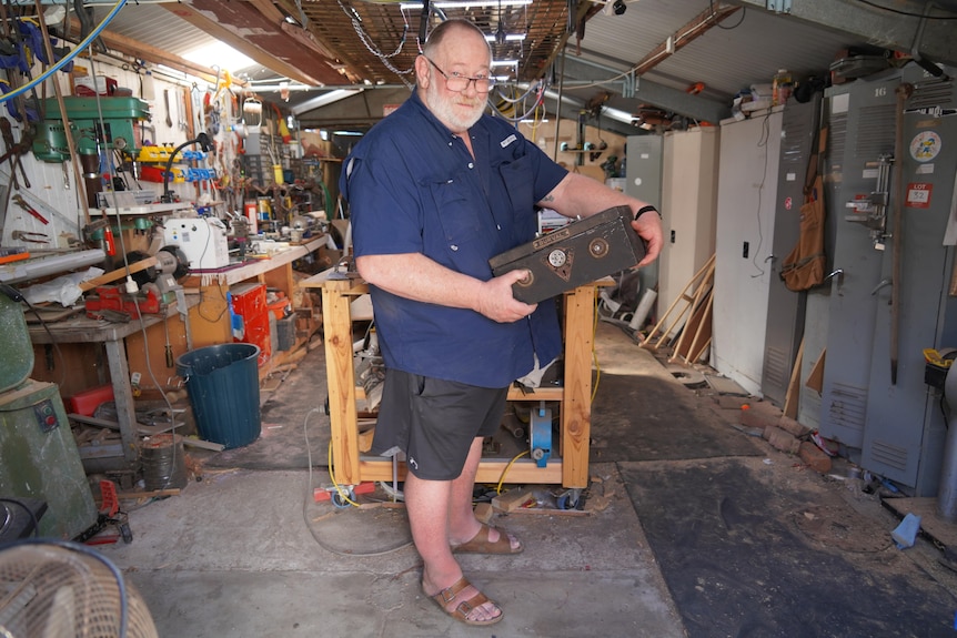 Un homme portant une chemise bleue et un short tient une boîte en métal dans un hangar