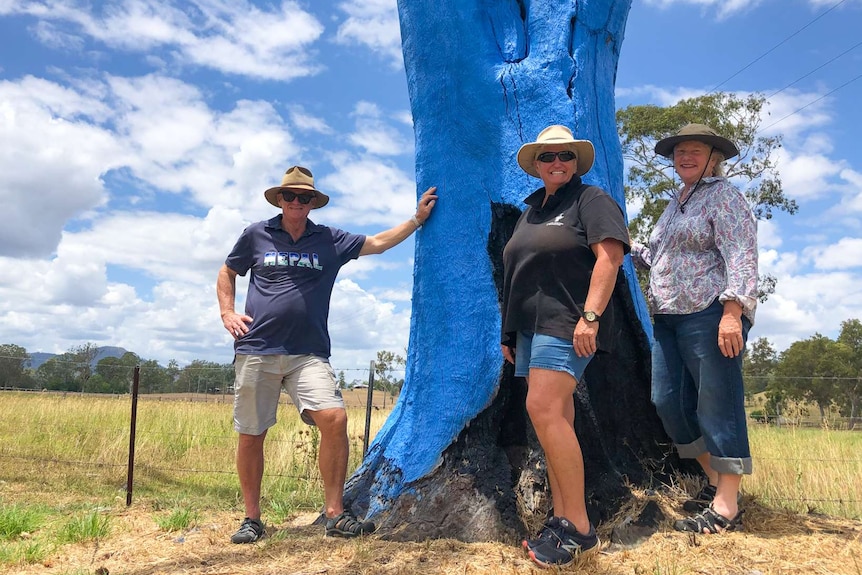 A tree painted blue with three people standing nearby.