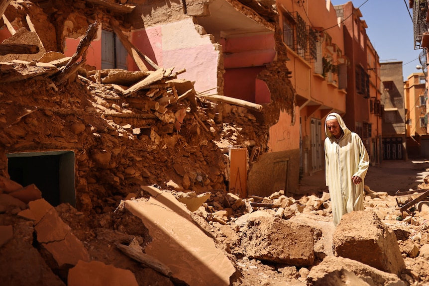 Man stands in front of crumbled home debris 