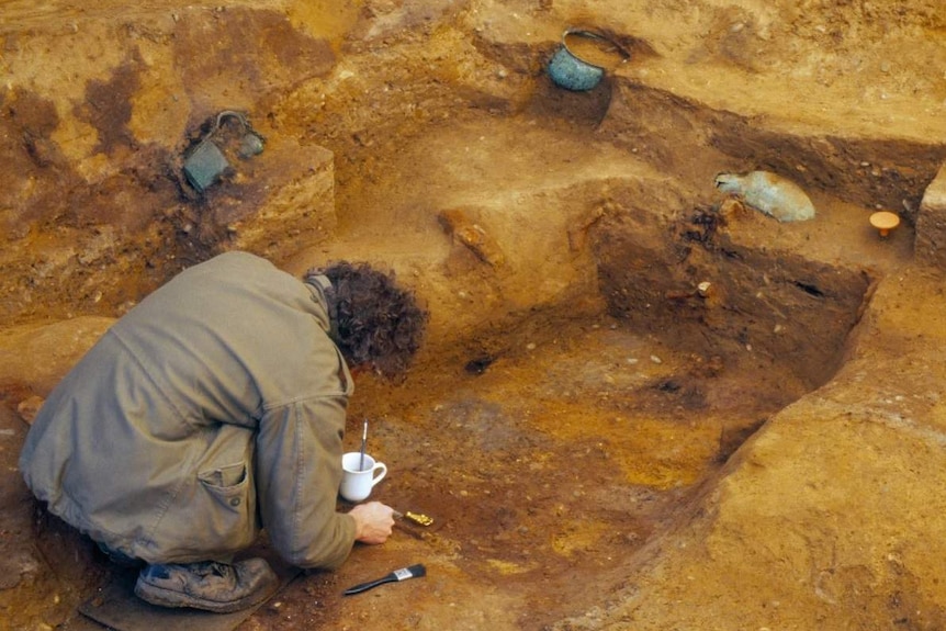 A man using tools and brushes at an archaeological site.