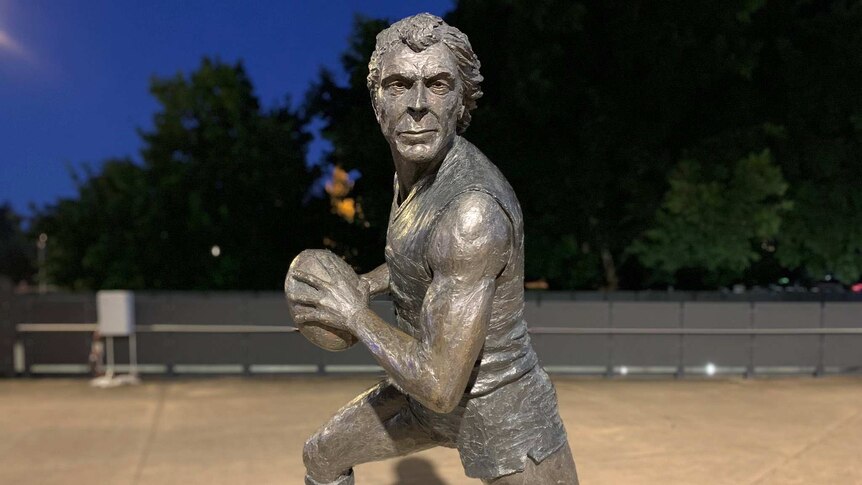 A metal statue of a man running while holding a football