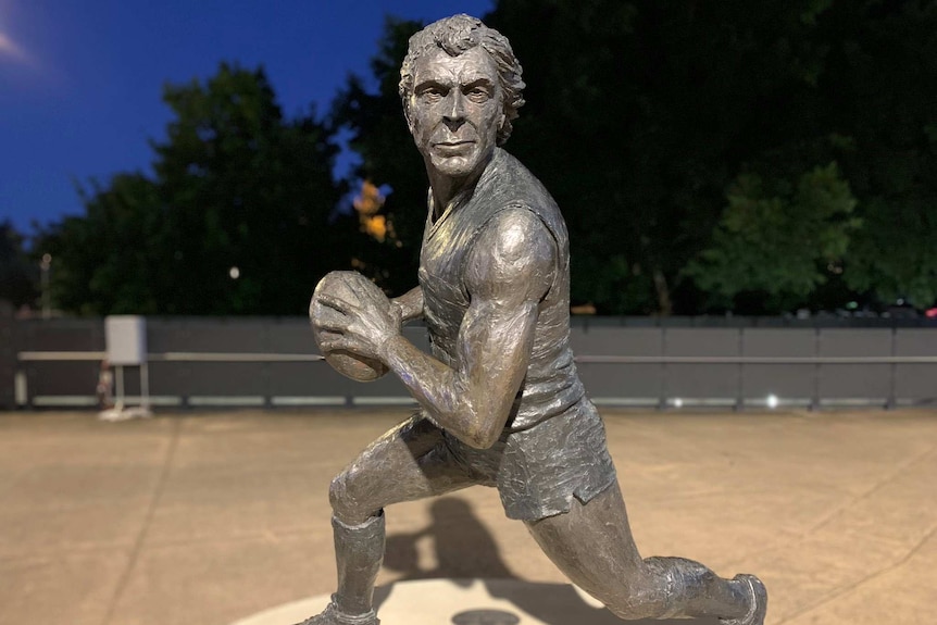 A metal statue of a man running while holding a football