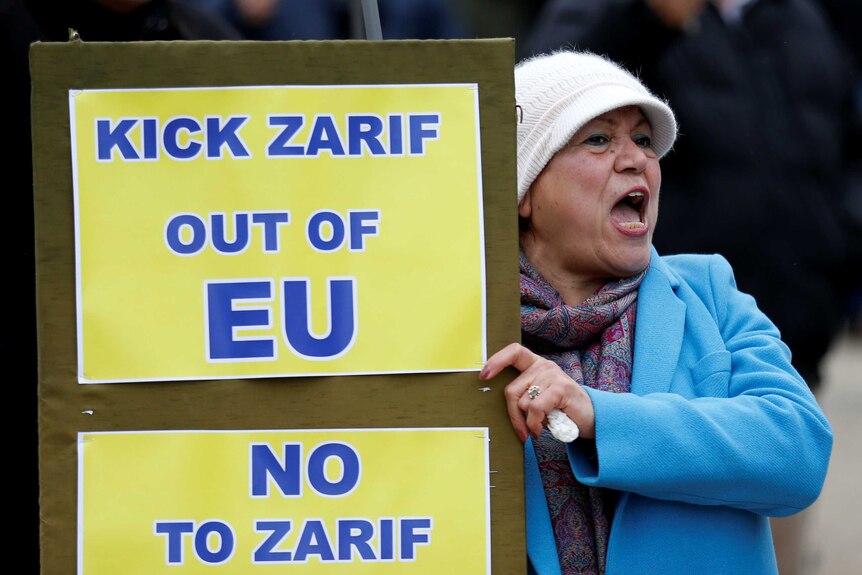 A woman chants and holds a protest sign.