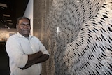 The Indigenous artist stands with his artwork, etched into an aluminium board