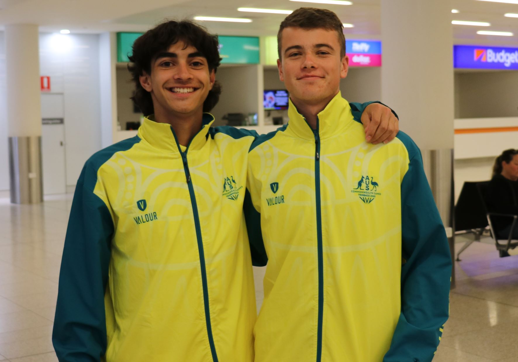 Two young men stand with their arms round each other wearing Australia tracksuits.