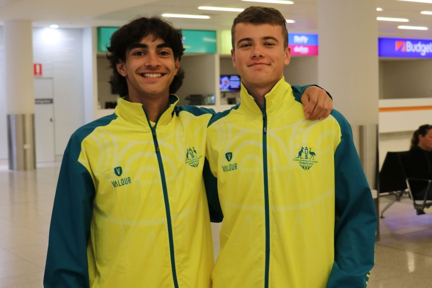 Two young men stand with their arms round each other wearing Australia tracksuits.