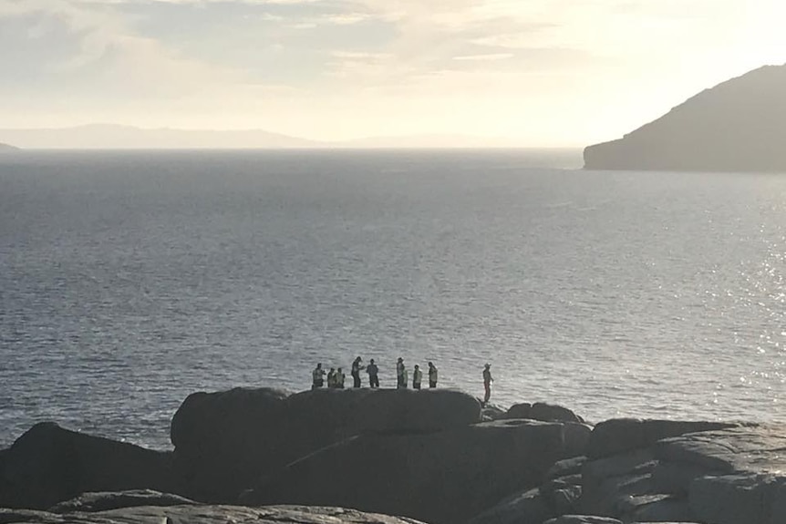 Police stand on the edge of a cliff with the sea in the background.