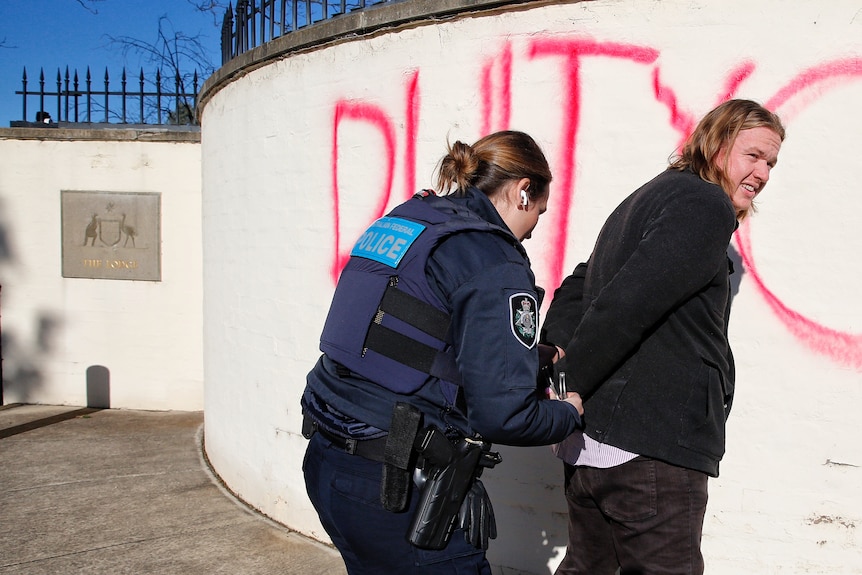 Police handcuff a protester outside The Lodge