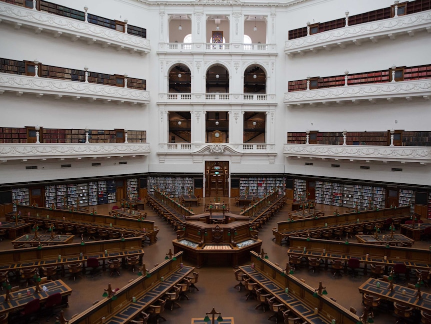 A view of empty desks and rows of bookshelves from above in the dome reading room.