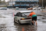 Man pushes car out of floodwater.