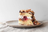 Slice of lamington cake with toasted coconut, cream, jam, fresh raspberries and chocolate ganache on a plate.