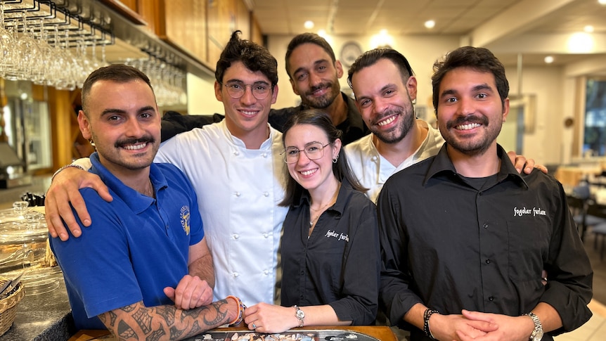 A group of six people standing close together at a bar