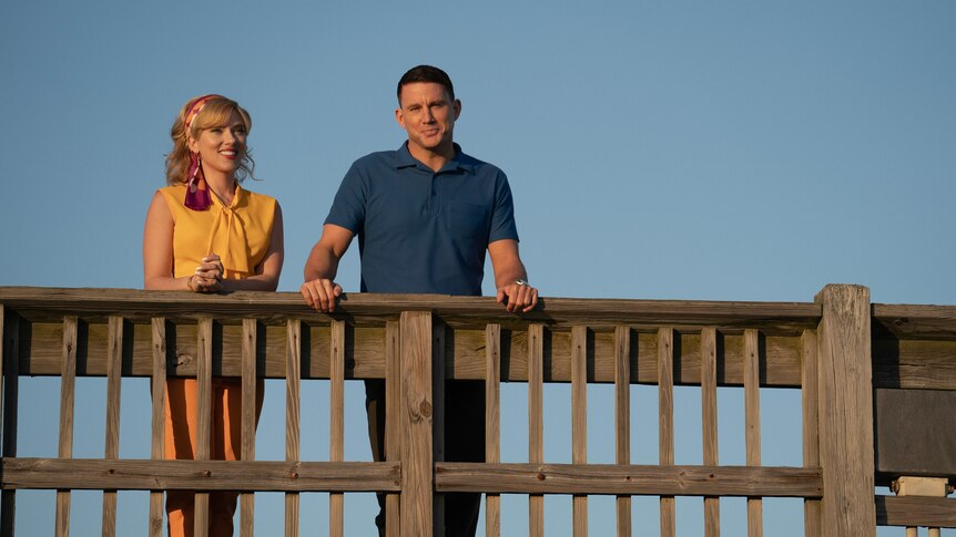 A still from the movie Fly Me to the Moon with Scarlett Johansson and Channing Tatum in 50s clothes standing on a wooden bridge