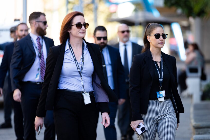 Two female WA Police detectives in plain clothes with lanyards on walk outside court in Perth in front of other male detectives.
