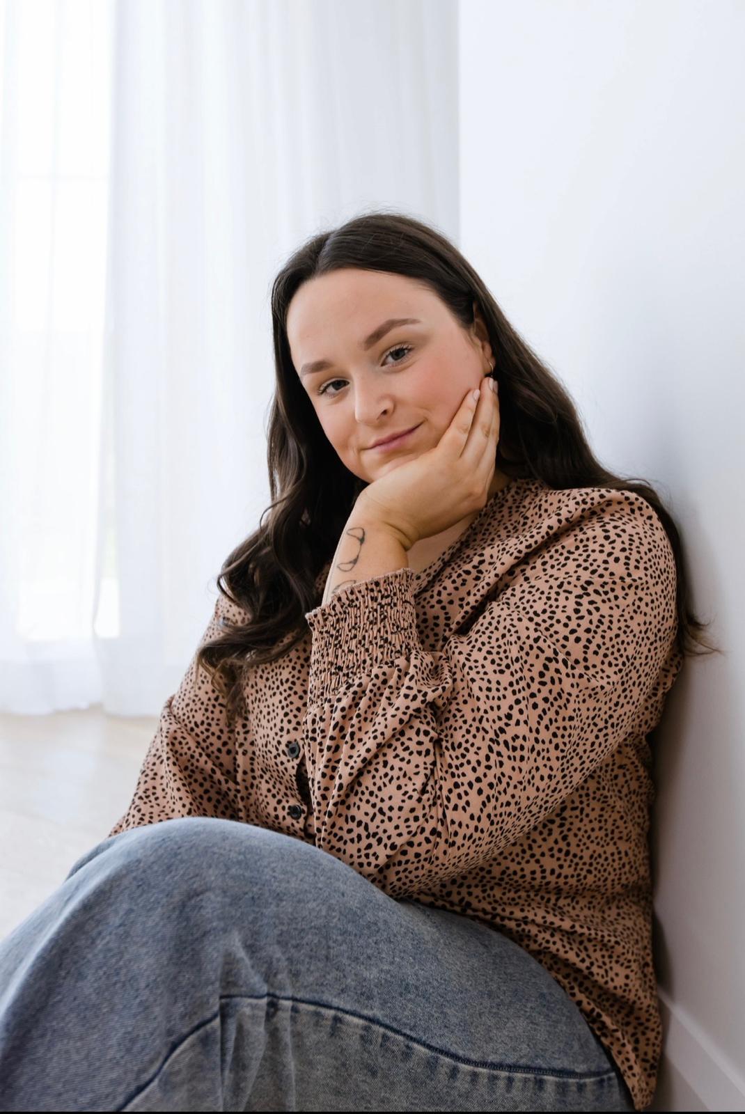 A woman with brown hair looks at the camera, resting her chin on her hand
