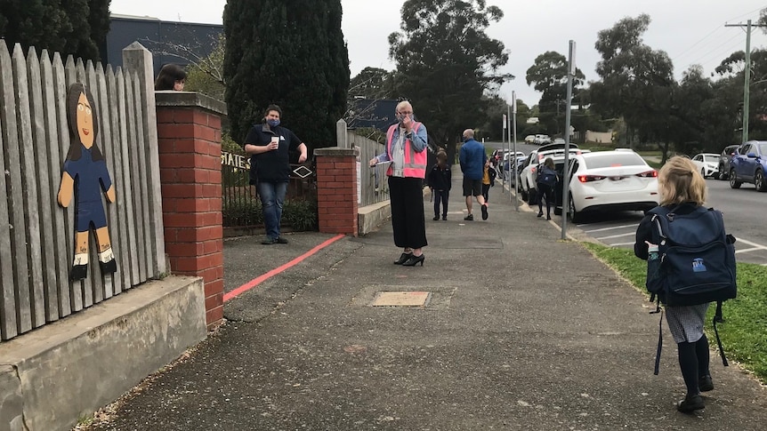 a child in a school uniform walks towards the school gate