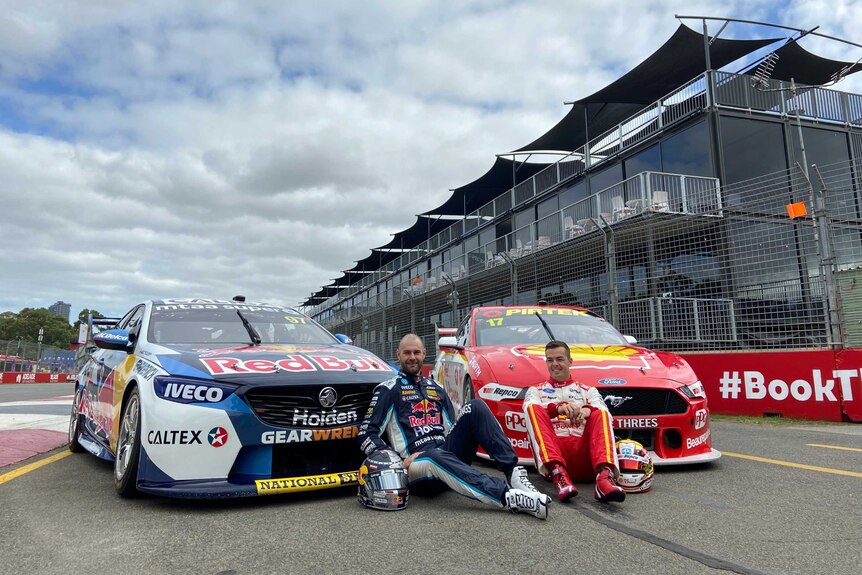 Shane van Gisbergen and Scott McLaughlin sit in front of two Supercars on a track.