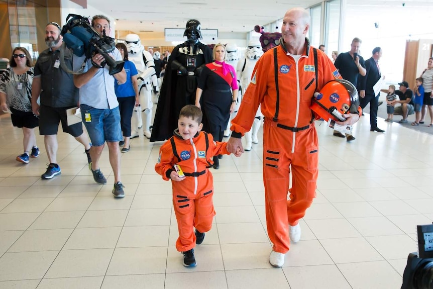 Dwayne and an astronaut in their space suits walking through Adelaide Airport.