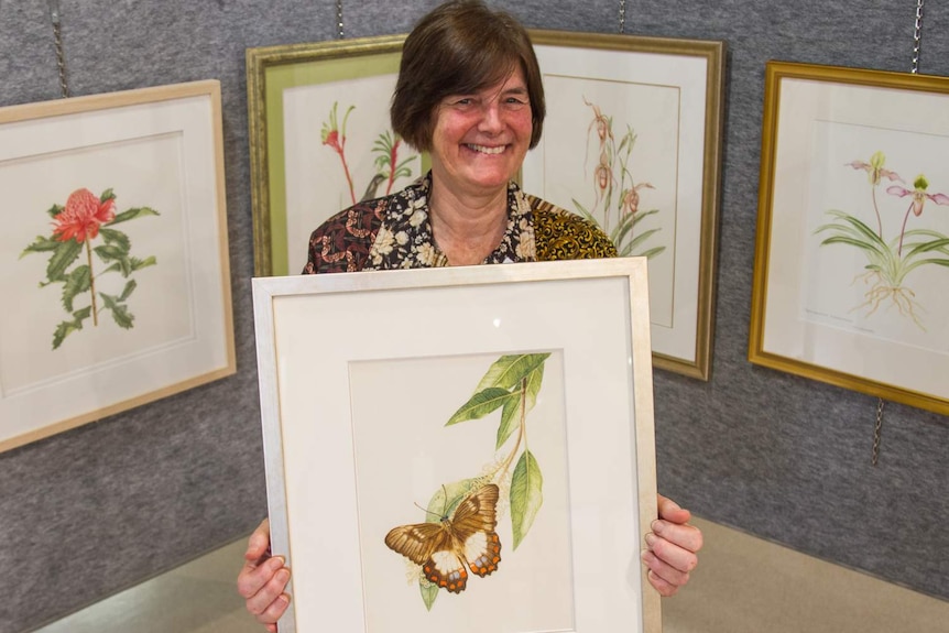 Dr Nita Lester holds framed art work of a plant and butterfly.