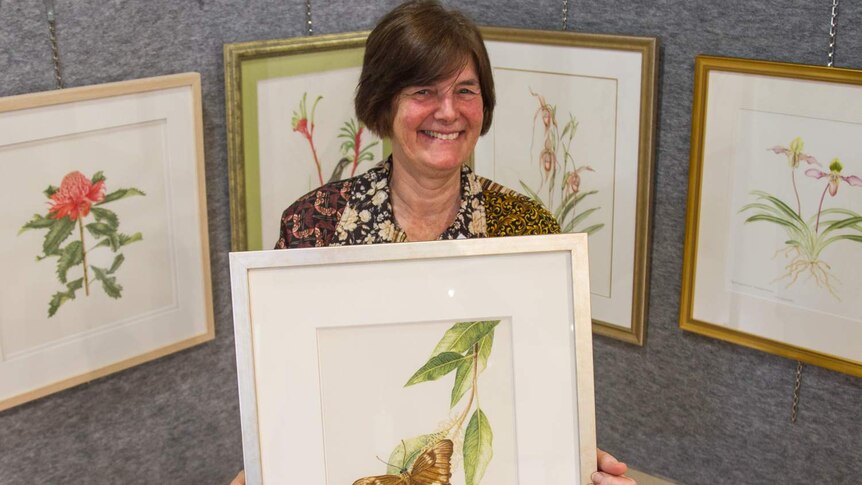 Dr Nita Lester holds framed art work of a plant and butterfly.