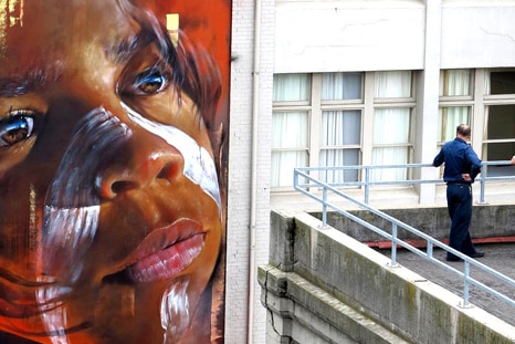 Two men look at a large portrait of an Indigenous child on a city building