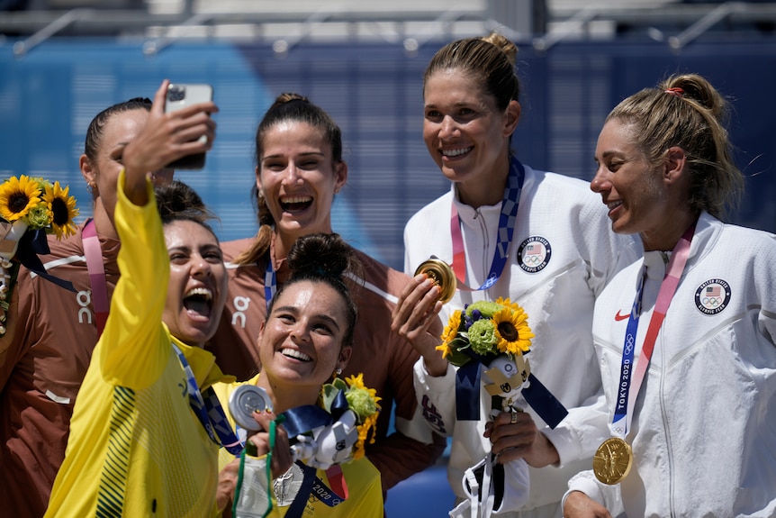 A grinning Australian beach volleyballer holds her phone to take a picture of her, her partner and the other Olympic medallists.