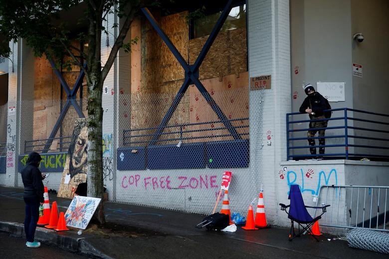 Two protesters stand on either side of a spray painted wall that says 'cop free zone' .