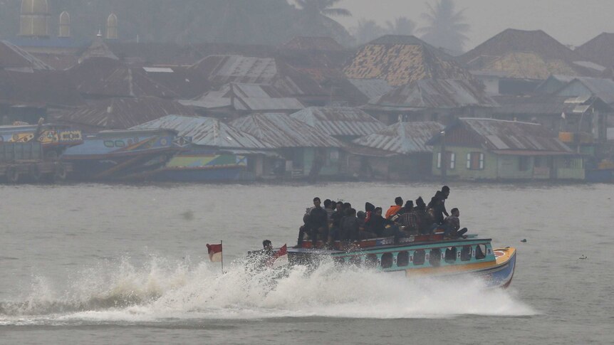 Passengers sit on the top deck of a wooden boat in Palembang