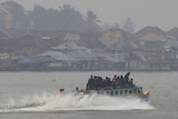 Passengers sit on the top deck of a wooden boat in Palembang