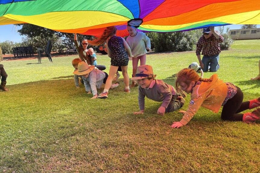 Young children crawl and play under a rainbow parachute at the Alice Springs ICPA's first playgroup at Ti Tree Grape Farm.