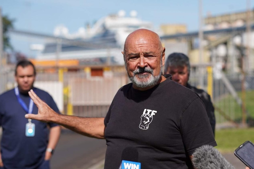 A man talks to reporters in front of a port