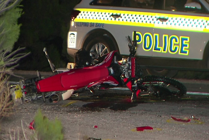A crashed motorcycle lays on the road next to a police car 