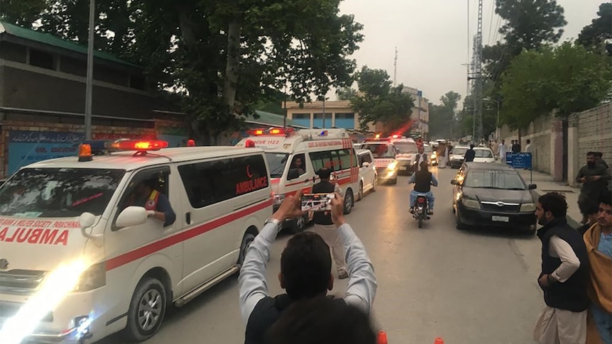 A man takes a smart phone photo of a string of ambulances on a busy city street
