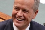 Bill Shorten looks into the distance and smiles while sitting in the Opposition leader's seat in Parliament House