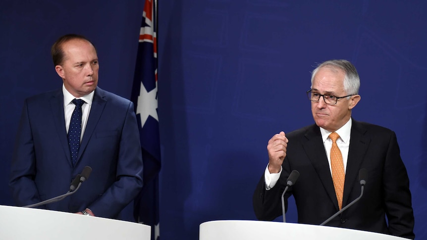 Peter Dutton looks at Malcolm Turnbull, who is answering a question with his hand raised, during a press conference.