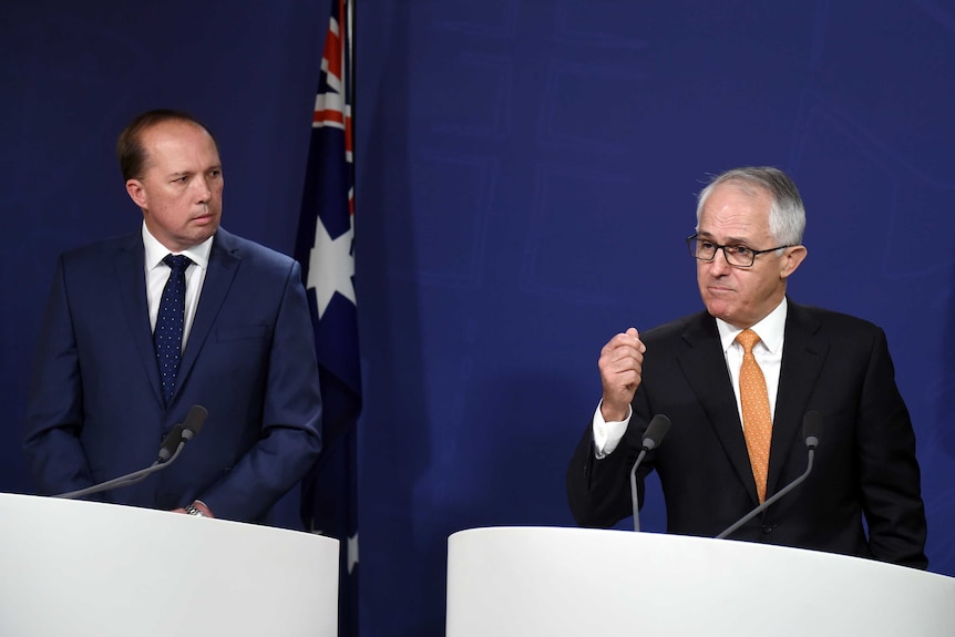 Peter Dutton looks at Malcolm Turnbull, who is answering a question with his hand raised, during a press conference.