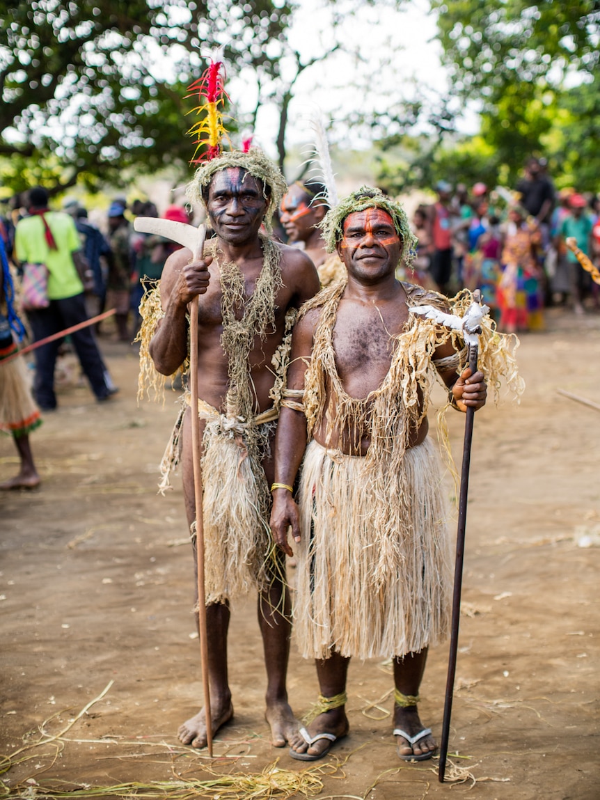 A portrait of two men wearing grass skirts and facepaint.