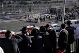 Orthodox Jewish people look at road where a section is blocked off by police