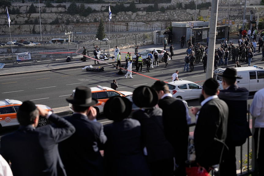 Orthodox Jewish people look at road where a section is blocked off by police