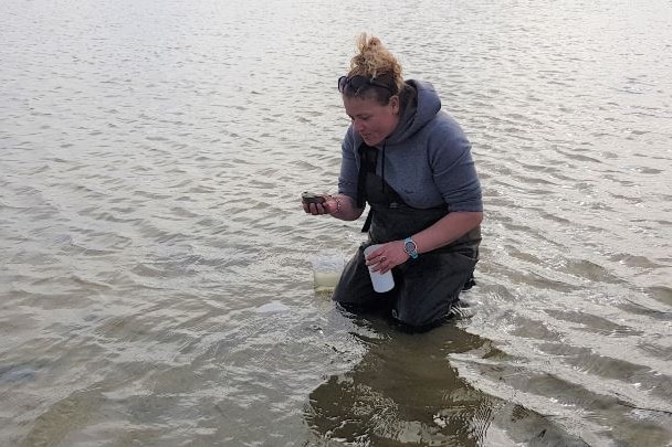 A woman holding a testing kit standing in water.
