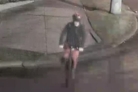 A person wearing what appears to be a mask over their face riding a bike taken from CCTV vision.