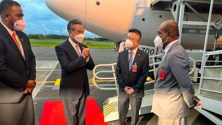 Four men greet each other on tarmac beside plane.