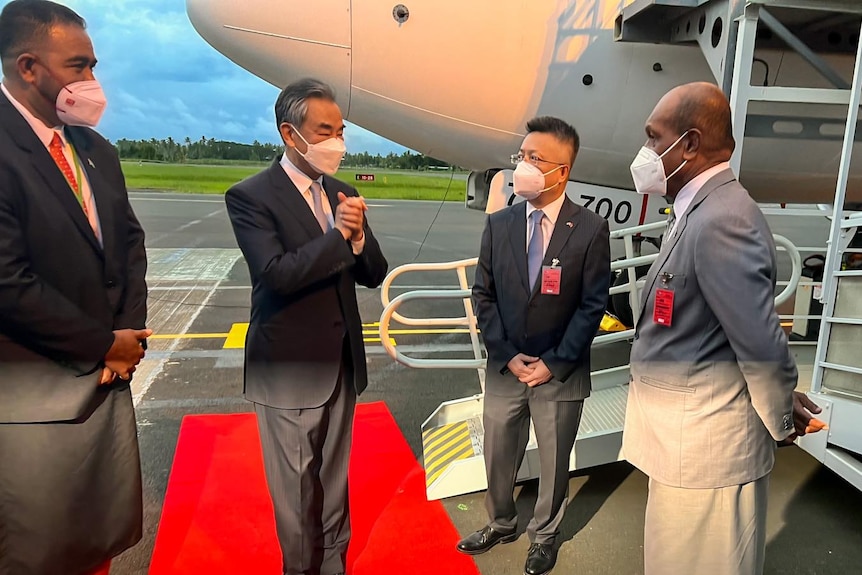 Four men greet each other on tarmac beside plane.