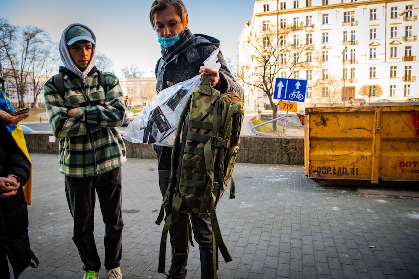 A man holds a backpack and clear bag filled with equipment.